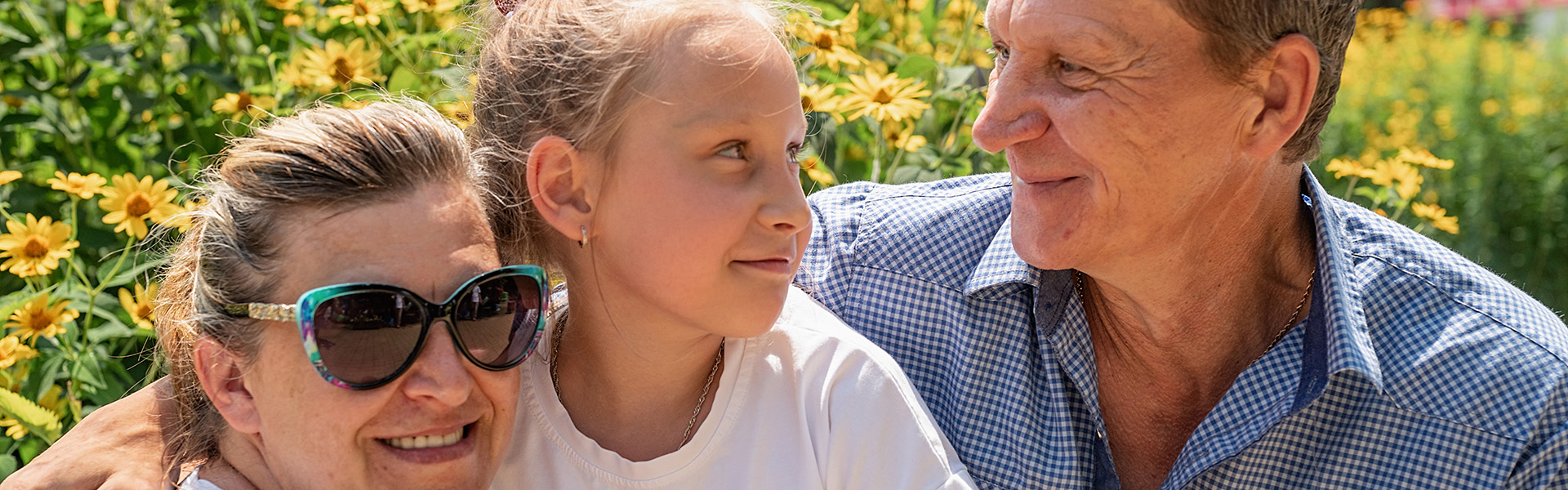 A little girl sat with her foster carers outside in the sun as she looks at her foster dad