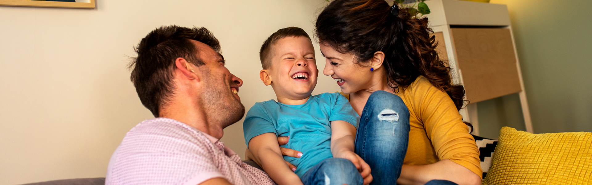Foster parents giggling with foster son on the sofa in their living room