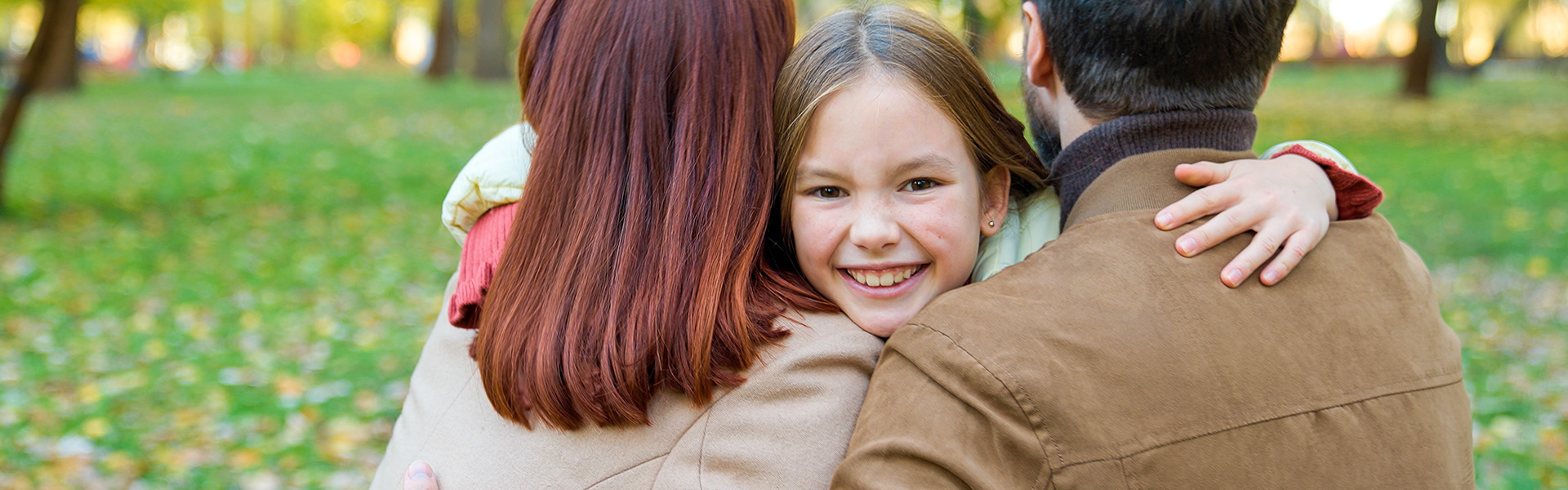 Child hugging foster mum and foster dad in the park