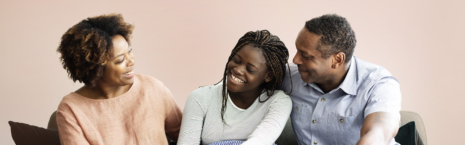Foster parents looking at their teenage foster daughter as she smiles at her foster mum while sitting on the sofa