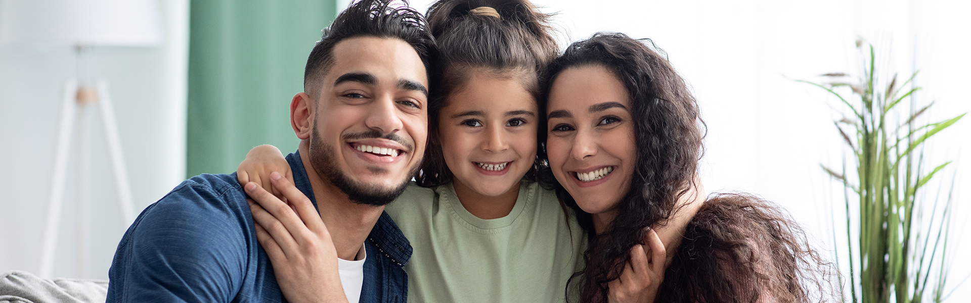 Young man and woman are smiling are the camera with a little girl between them with her arms around their shoulders