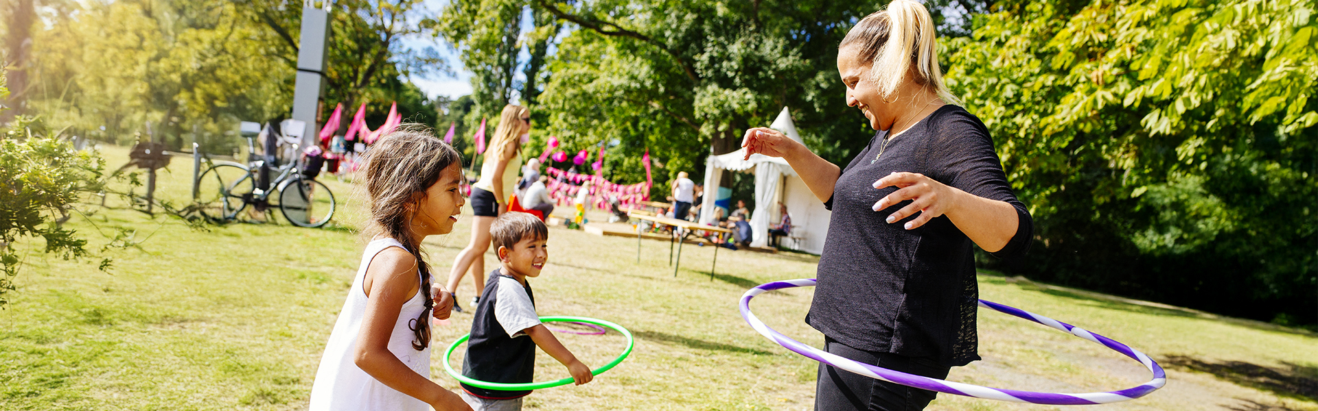 Middle aged woman hoola hoops with a young boy and a young girl at a summer festival