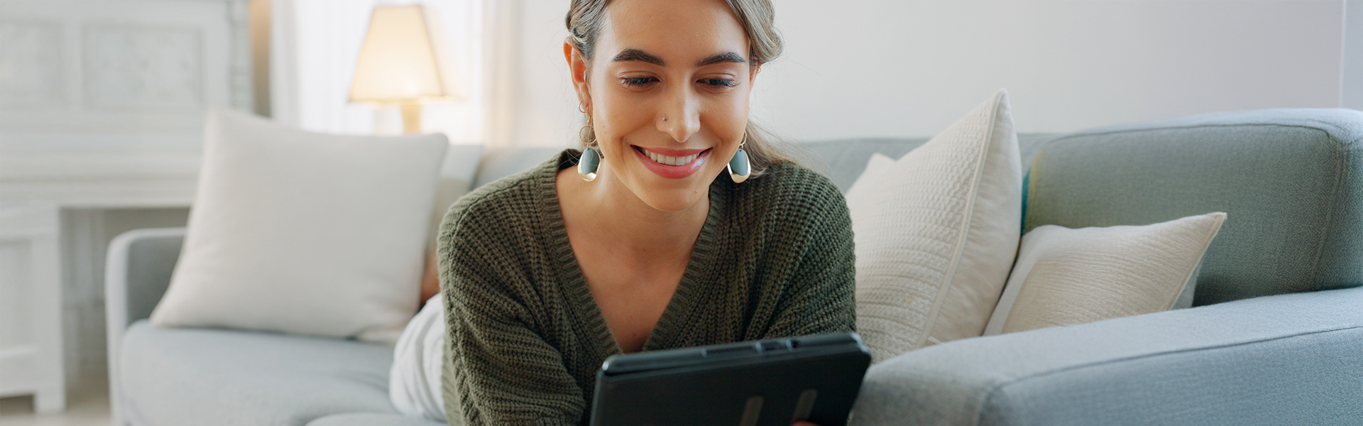 Woman layed on her sofa scrolling on a tablet while smiling