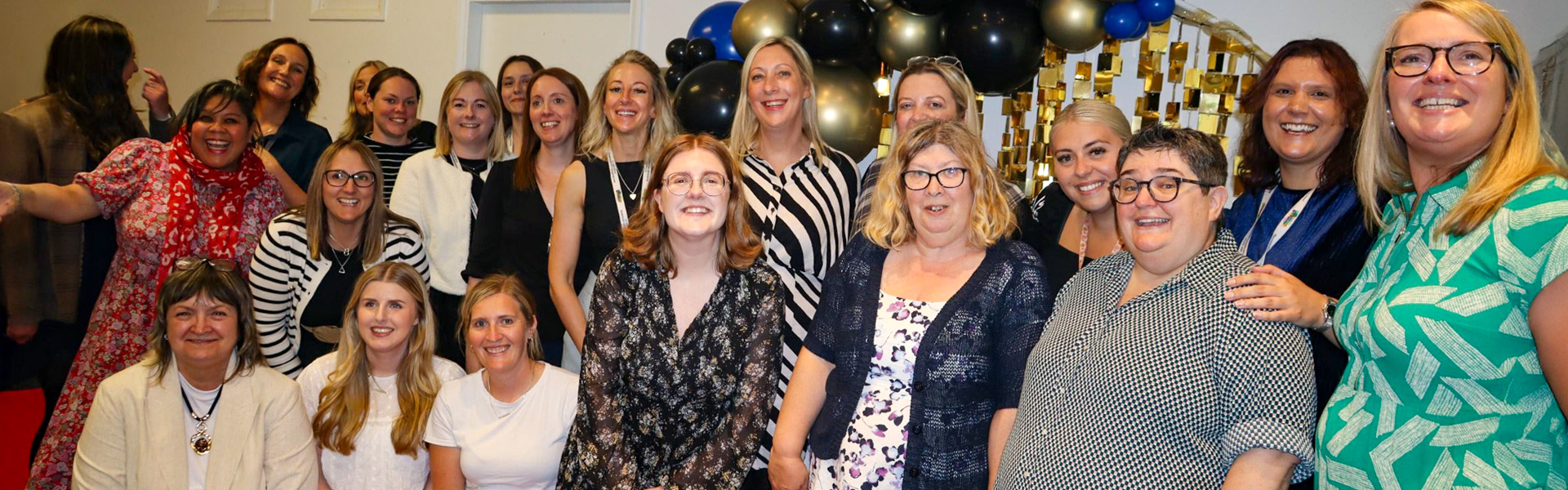 Group of people stood in front of a balloon arch smiling