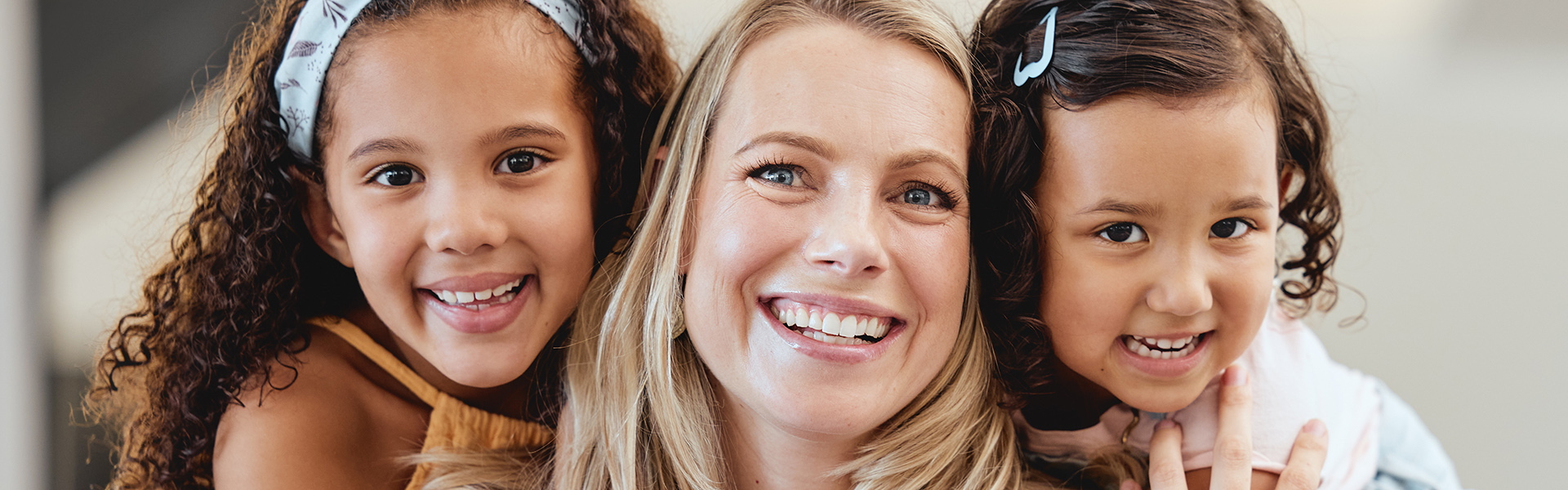 Middle aged foster mum smiling at the camera as she hugs two foster children