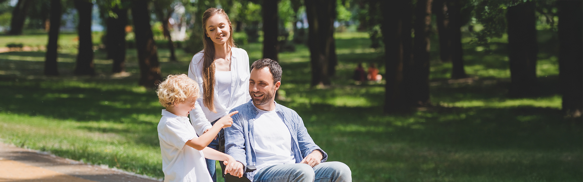 Foster mum pushing foster dad in a wheelchair while he holds their foster son's hand
