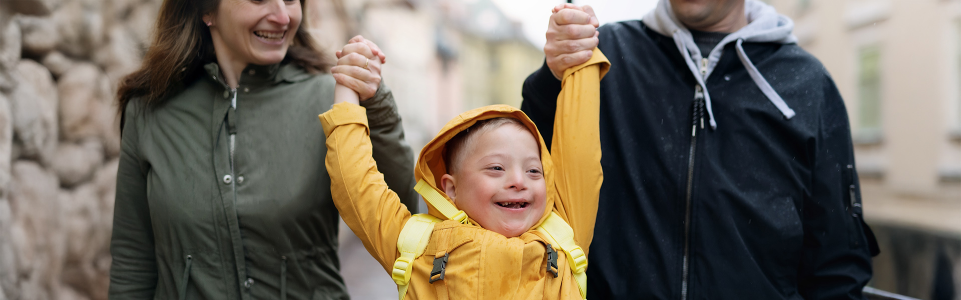 Young boy with down sydrome is smiling as his foster carers swing him in the air