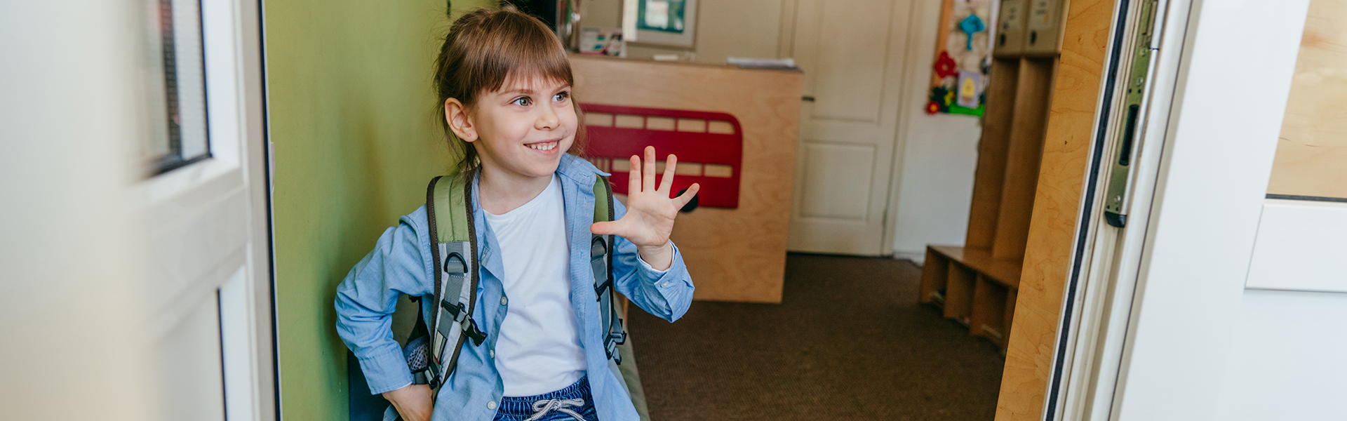 Happy little girl with backpack standing near the door at school