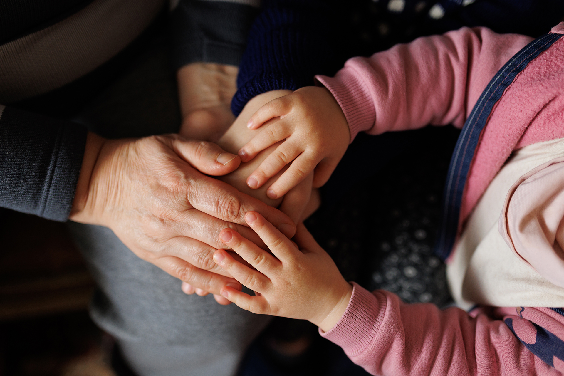 Close up photo a seniors wrinkled hands clasped with a childs