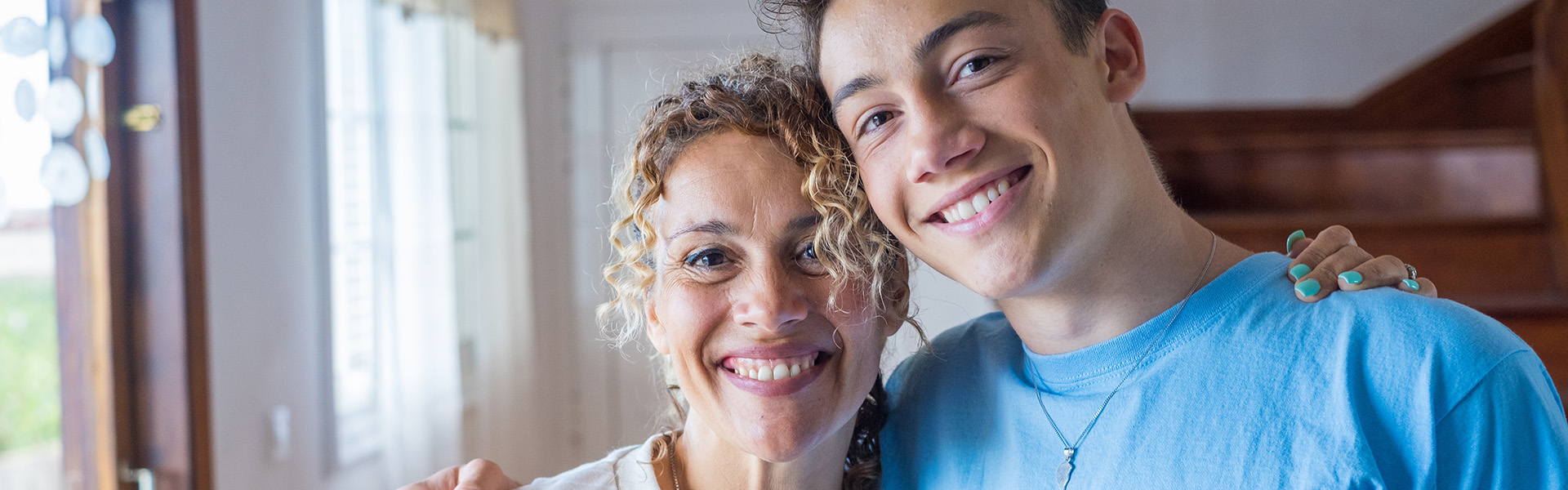 MIddle aged foster mum smiling at the camera as she hugs her teenage foster son