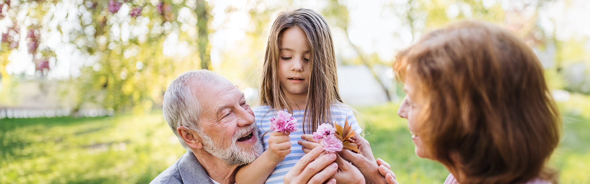 Older couple crouching down with young girl as they pick flowers in the park